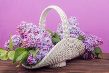 Beautiful White Vintage Wicker Basket On A Wooden Table. Lilac Flowers In A Retro Basket