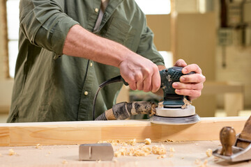 close-up hands of joiner worker using electric sander in workshop. Joiner sanding wooden board on table. Carpentery work. Small Business Concept. Copy space