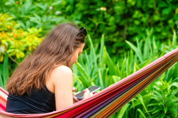 Wall Mural - gorgeous girl with sunglasses sitting on a hammock, relaxing and using a smartphone