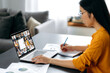© Kateryna - Side view at asian female student watching lesson online and studying distantly. Young woman takes notes, listening lecture from female teacher on video call.Video conference with teacher and students