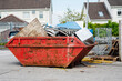 Red garbage removal skip full of rubbish and ready for collection in a street. Old dumpster full of junk in a yard. Waste industry in urban enviroment
