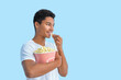 African-American teenager eating popcorn on color background