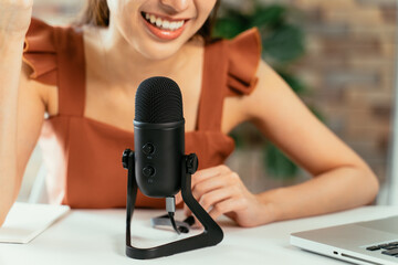 Closeup of young beautiful woman smiling sitting on desk using laptop and mic recording podcast while taking interview