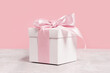 White gift box with shining pink ribbon bow on pink background. Gift or holiday concept. Mothers Day, birthday wedding or St Valentines day banner with copy space