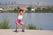 Strong woman doing exercises with portable and elastic pilates exercise stick for full body workout near by the lake