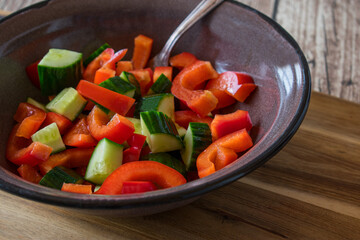 Wall Mural - Salad with cucumbers and red peppers marinated in olive oil and served in a rustic enamel bowl with fork