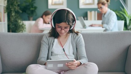 Wall Mural - Video of little girl listening to music with digital tablet while her mother and sister working in living room at home.