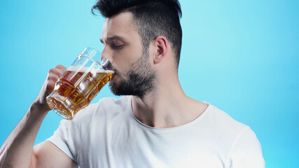 young man drinking cold beer isolated on blue