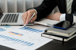 © PaeGAG - Businessman holding pen and pointing paper chart summary analyzing annual business report with using laptop at room office desk.
