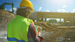© M-Production - Builder with documents on the background of a road junction construction site.