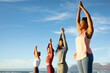 © Wavebreak Media - Group of diverse female friends practicing yoga, standing and rising hands at the beach
