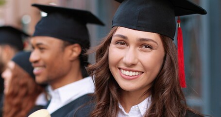 Happy times. Portrait view of the brunette happy girl looking to the camera with wide smile while standing with her group mates and listening final speech from her teacher. Education concept