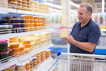 mature man choosing sauerkraut and pickles in supermarket