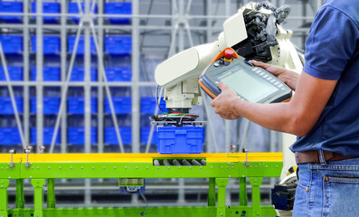 Close-up half body part of technician who using wireless remote to setting program for control robotic to work on industrial logistic smart factory, industry 4.0