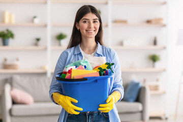 Wall Mural - Cheerful young housewife holding bucket with cleaning supplies tools