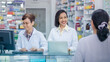 © SHUTTER DIN - Smiling friendly two young female pharmacist, standing at the counter and patient back in pharmacy