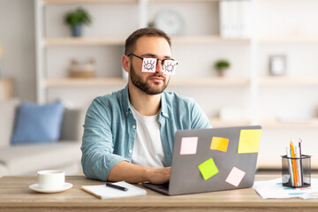 Poster - Tired millennial guy having stickers with drawings of open eyes on glasses, sleeping in front of laptop at home office