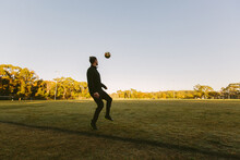 Whole Body Shot Of A Young Man On The Field Kicking A Ball In The Air
