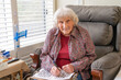 © Austockphoto - An elderly lady sitting in a chair doing a crossword and smiling