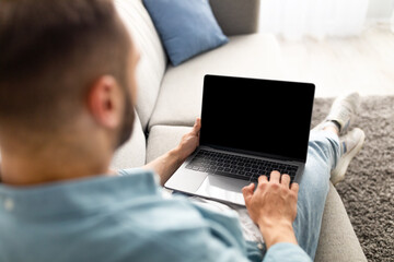 Poster - Unrecognizable young man using laptop on comfy sofa at home, mockup for website design on screen