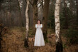 © Milou Dirks - Woman in long white dress standing in forest in autumn or winter hiding her face