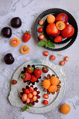 Wall Mural - Vertical composition. Juicy ripe berries and fruits on metal plates on a gray textured background. View from above.