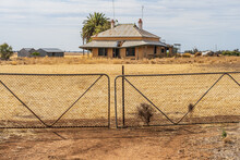 Closed Double Gates In Front Of An Old Abandoned Farmhouse In The Middle Of A Paddock