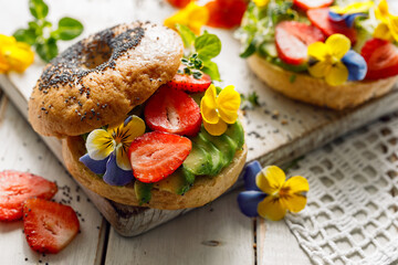 Wall Mural - Close up view of a vegan bagel sandwich with edible pansy flowers, strawberries and avocado. A healthy and beautiful breakfast