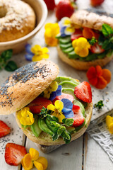 Wall Mural - Bagel sandwich with addition avocado slices and edible pansy flowers, close up view. Delicious and beautiful vegan food