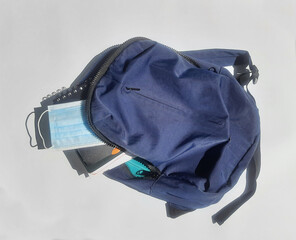 A blue backpack full of notebooks  and a mask on a grey background 