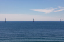 Three Wind Turbines Out On The Horizon And On A Calm Ocean