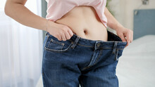 Beautiful Young Woman With Flat Stomach Posing In Front Of Mirror Wearing Old Large Jeans. Concept Of Dieting, Loosing Weight And Healthy Lifestyle.