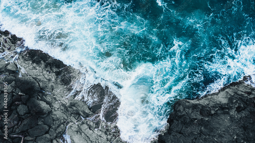 Drone shot of ocean waves clashing into dark rocks - obrazy, fototapety, plakaty 