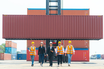 Portrait Of man woman Engineers and asian Factory workers walking in front of machine lift container and cargo space. Business people with confident and smart working in shipping transport industry.