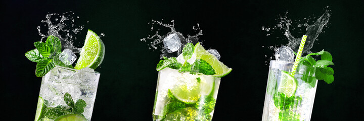 Wall Mural - Glasses of Mojito with splashes and flying ice cubes on black and green background in bar | Limes, water, drops