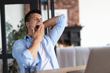 Exhausted young Caucasian man yawns, feels tired and sleepy after a long day at work, need rest concept