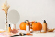 Pumpkins and bottles of cosmetic products on light background