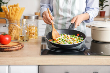 Woman cooking tasty rice with vegetables on stove in kitchen, closeup