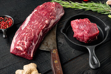 Wall Mural - Fresh and raw beef meat. Whole piece of tenderloin with steaks and spices ready to cook, in cast iron frying pan, on black wooden table background