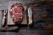 Rare rib eye steaks with herbs and spices, on wooden serving board, with meat knife and fork, on old dark  wooden table background, with copy space for text