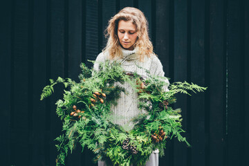 Woman in knitted sweater holding wreath. Festive decoration.