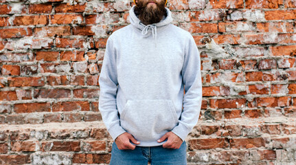 Wall Mural - City portrait of handsome hipster guy with beard wearing gray blank hoodie or sweatshirt and hat with space for your logo or design. Mockup for print