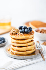 Wall Mural - Stack of pancakes served with maple syrup, blueberries and walnuts on a plate, closeup view, white background