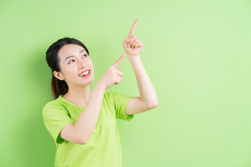 Young Asian woman wearing green shirt and posing on green background