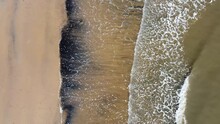 A Drone Shot Looking Straight Down On Waves Crashing On A Beach In And Ex-mining Area With Black Coal Dust Being Pushed Up Onto The Sand