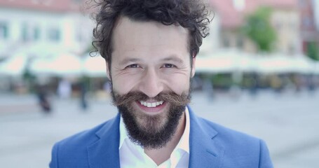 Poster - close up of attractive bearded guy with long moustache and curly hair smiling when camera is zooming in in front of medieval city background outdoor