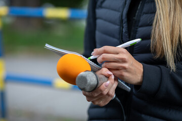 News reporter or TV journalist at press conference, holding microphone and writing notes