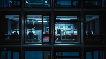 Poster - Shot from Outside the Window: Businessmen and Businesswomen Working in the Office. Managers and Specialists Doing Financial Business in the Evening. Employees Work on Computers and Delegate Tasks.