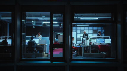 Poster - Shot from Outside the Window: Businessmen and Businesswomen Working in the Office. Managers Doing Financial Business in the Evening. Employees Work on Computers, Laptops, Mobile Phones, Tablets.