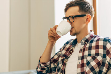 young business man in glasses drinking aromatic coffee from a cup sitting in a cafe near the window